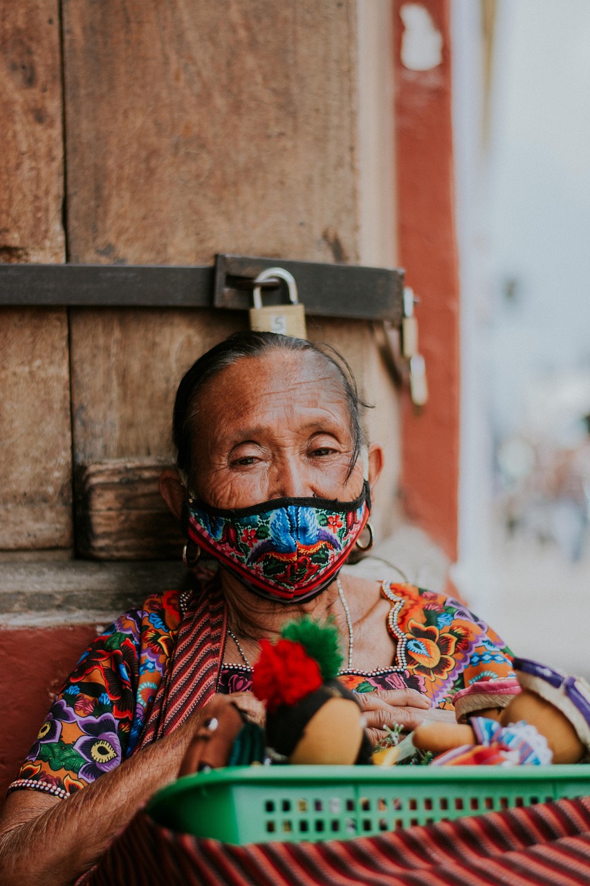 potrait of an old sitting woman wearing a colorful weaved dress and a face-mask